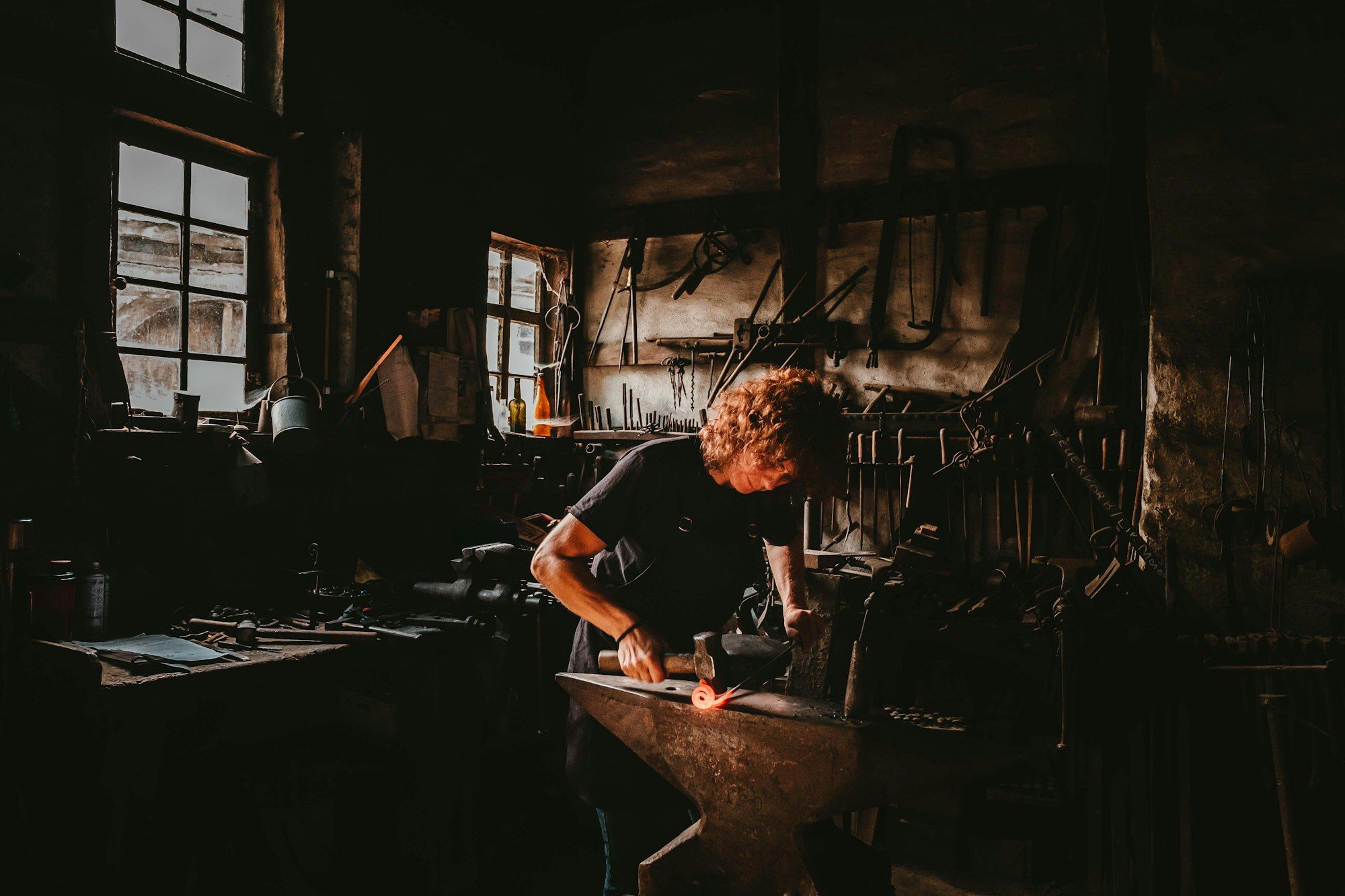 A blacksmith striking hot metal on an anvil inside a forge workshop