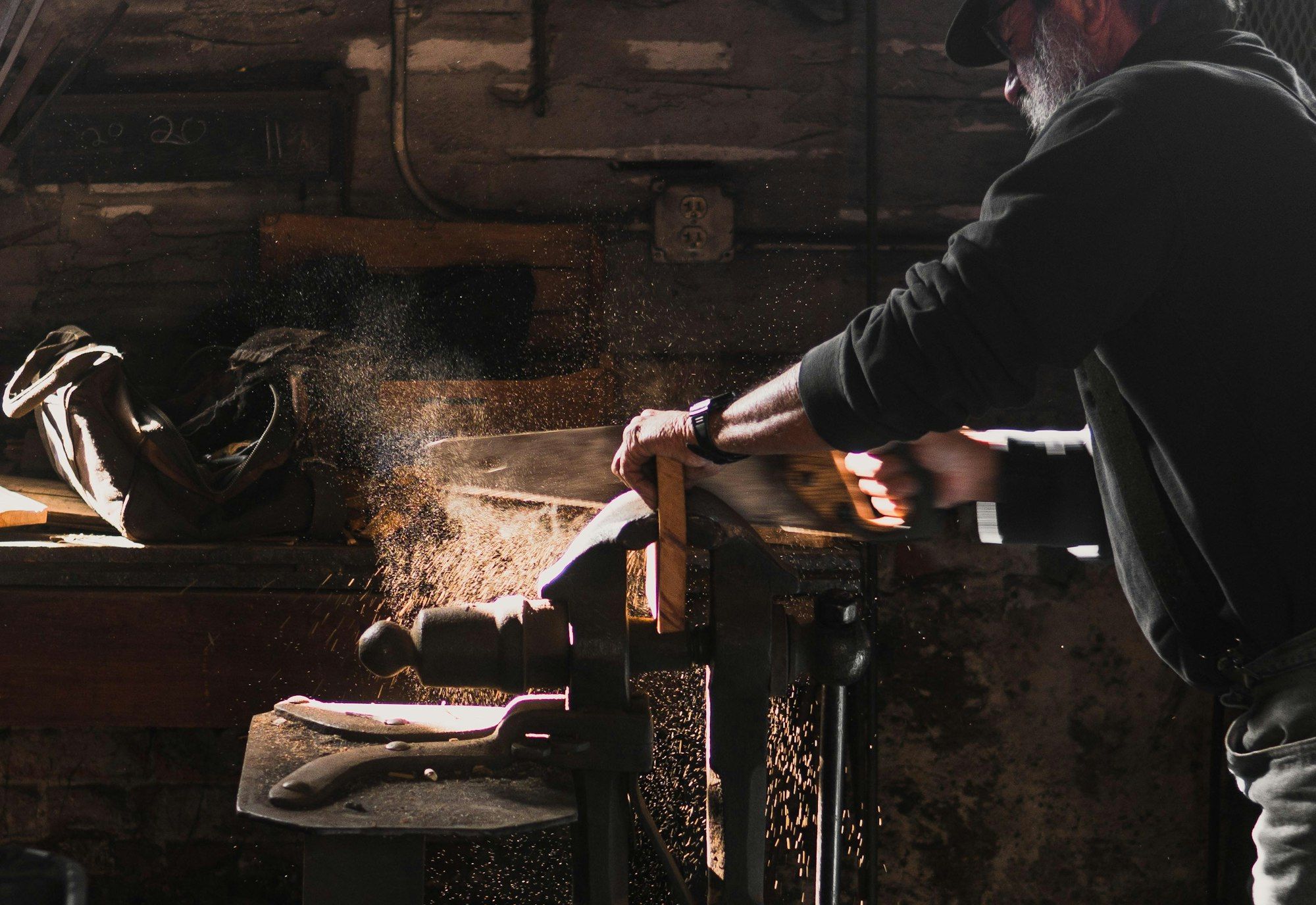 A woodworker sawing timber at a bench in his workshop